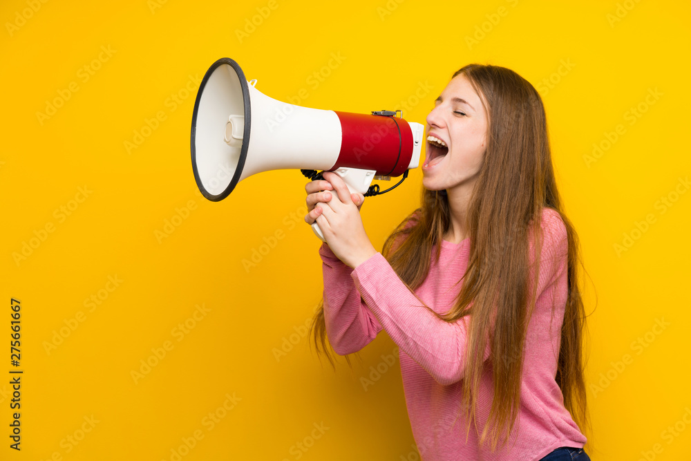 © luismolinero - Young woman with long hair over isolated yellow wall shouting through a megaphone