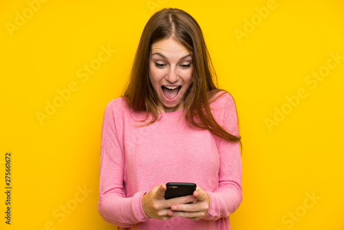 Young woman with long hair over isolated yellow wall surprised and sending a message