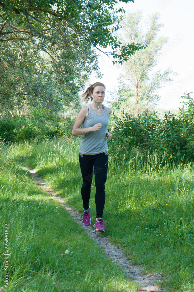 Beautiful, athletic, slender woman with headphones and sports suit runs through the park, summer, sunny morning. Morning jogging and sports Beautiful, athletic, slender woman with headphones and sports suit runs through the park, summer, sunny morning. Morning jogging and sports