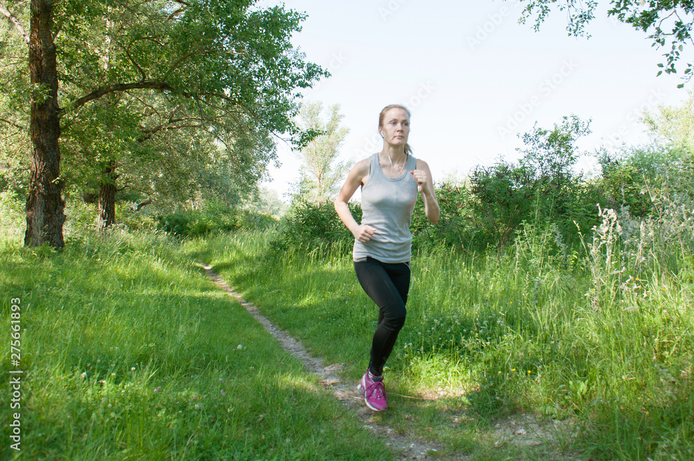 Beautiful, athletic, slender woman with headphones and sports suit runs through the park, summer, sunny morning. Morning jogging and sports Beautiful, athletic, slender woman with headphones and sports suit runs through the park, summer, sunny morning. Morning jogging and sports