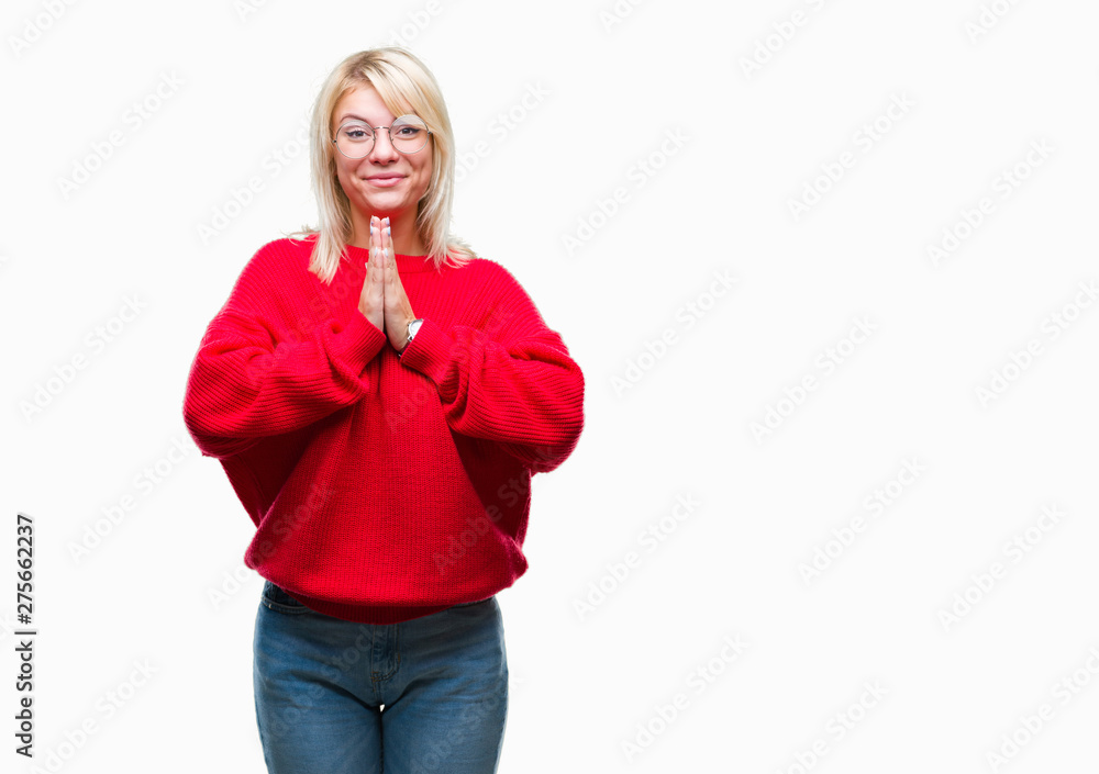 Fototapeta premium Young beautiful blonde woman wearing sweater and glasses over isolated background praying with hands together asking for forgiveness smiling confident.