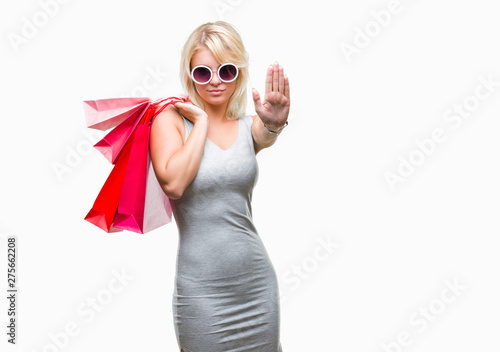 Young beautiful blonde woman shopping holding shopping bags on sales over isolated background with open hand doing stop sign with serious and confident expression, defense gesture