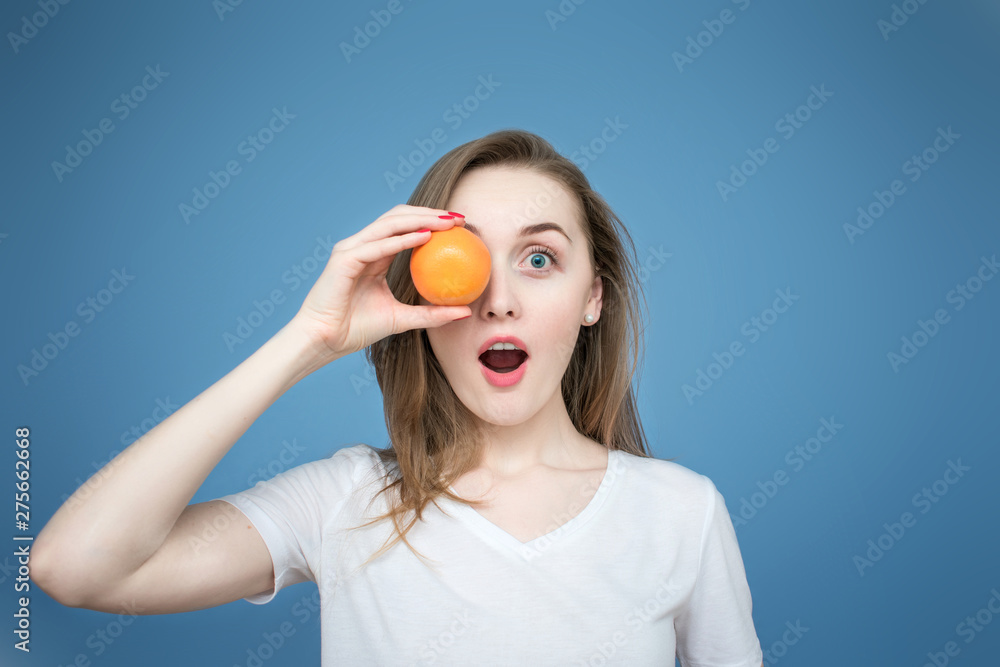 Young beautiful girl model with oranges on blue background, holding the orange near the face, mouth open in surprise and delight Young beautiful girl model with oranges on blue background, holding the orange near the face, mouth open in surprise and delight