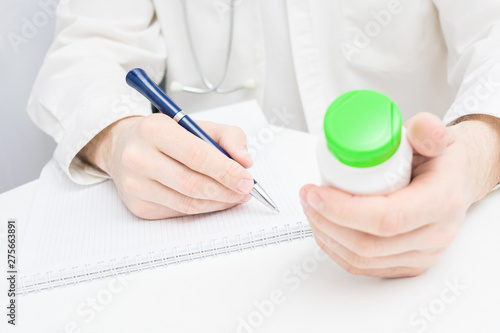 Doctor or physician writing prescription, holds in hand a medicine, close up