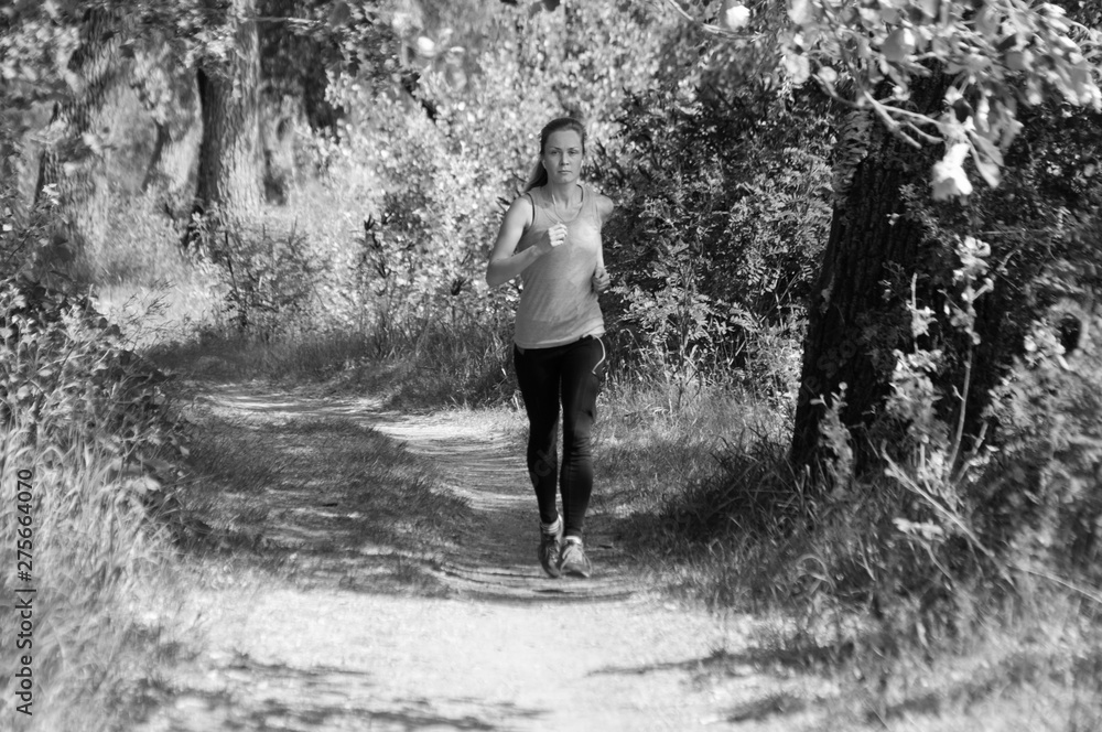 Fototapeta premium Athletic, beautiful girl runs in the park and listens to music, sunny summer morning, bw