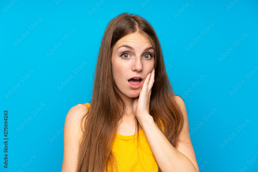 Young woman with long hair over isolated blue wall surprised and shocked while looking right Young woman with long hair over isolated blue wall surprised and shocked while looking right