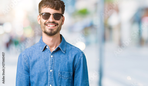 Young handsome man wearing sunglasses over isolated background with a happy and cool smile on face. Lucky person.