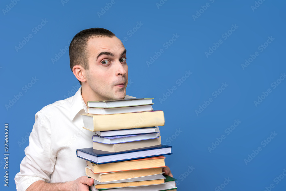 Portrait, young man in the white shirt with books, looking at the camera, blue background, front view, copy space, the concept of heavy loads in education Portrait, young man in the white shirt with books, looking at the camera, blue background, front view, copy space, the concept of heavy loads in education