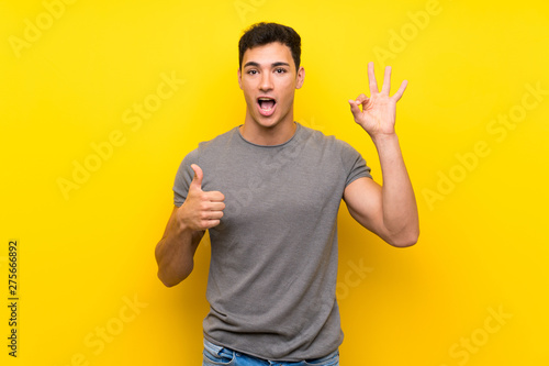 Handsome man over isolated yellow wall showing ok sign and thumb up gesture