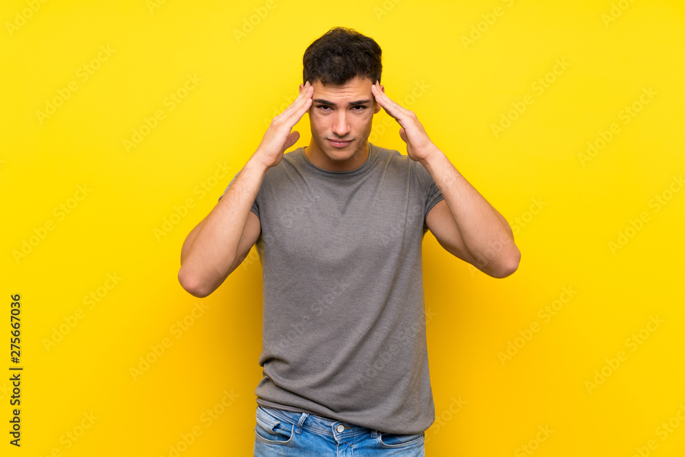 Handsome man over isolated yellow wall with headache Handsome man over isolated yellow wall with headache