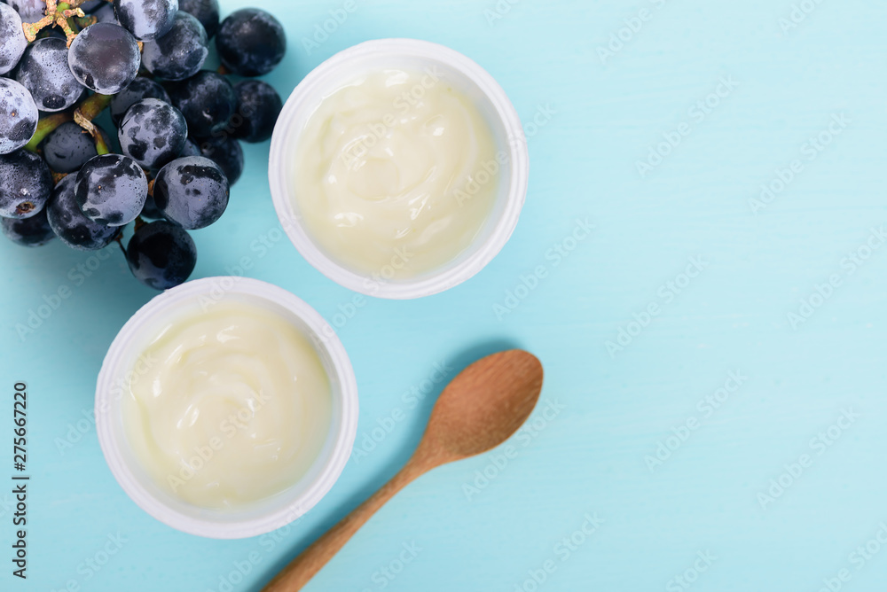 Two plastic cups of yoghurt with wooden spoon and grape on pastel background, healthy eating, top view Two plastic cups of yoghurt with wooden spoon and grape on pastel background, healthy eating, top view