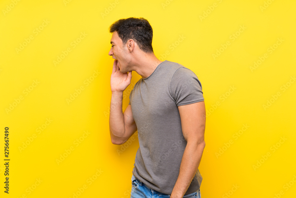 Handsome man over isolated yellow wall shouting with mouth wide open to the lateral Handsome man over isolated yellow wall shouting with mouth wide open to the lateral