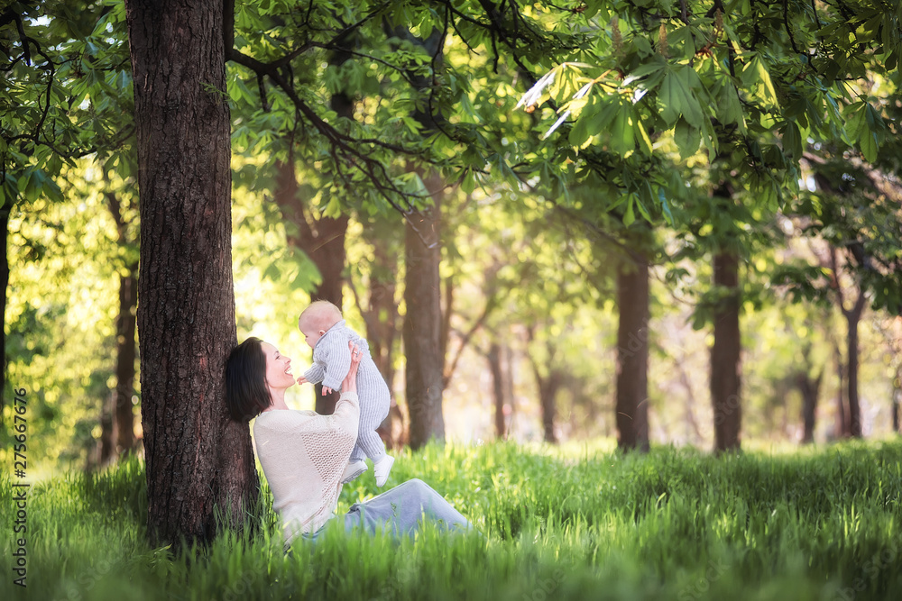 Young beautiful mother holds the baby in her arms in a green park. Baby under the protection of the mother. Young beautiful mother holds the baby in her arms in a green park. Baby under the protection of the mother.