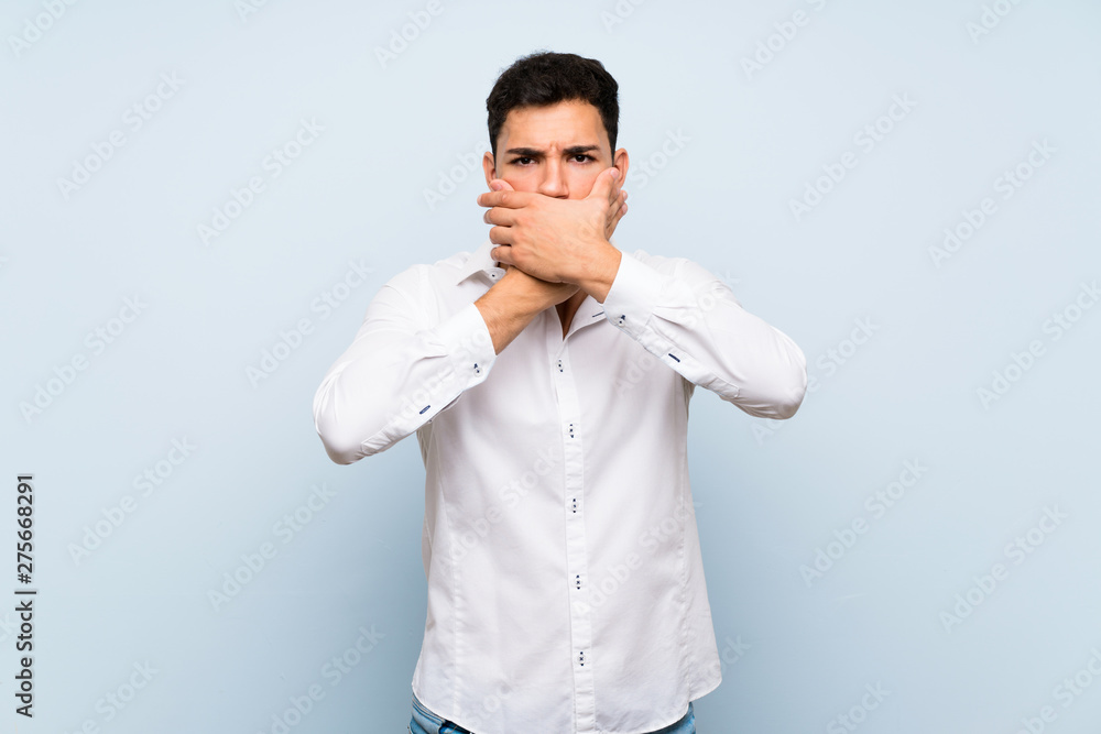 Handsome man over blue wall covering mouth with hands Handsome man over blue wall covering mouth with hands