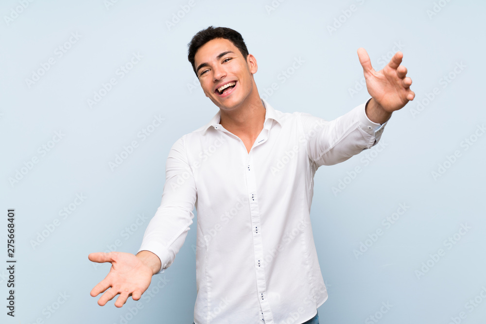 Handsome man over blue wall presenting and inviting to come with hand Handsome man over blue wall presenting and inviting to come with hand