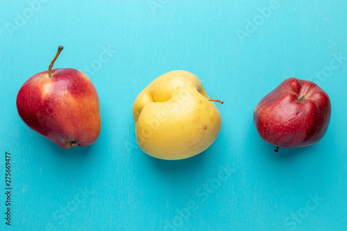 Three ugly apples are lying in row on turquoise painted wooden background.