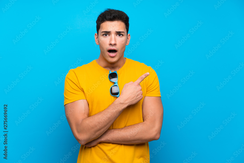 Handsome man over blue background surprised and pointing side Handsome man over blue background surprised and pointing side