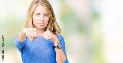 Fototapeta Naklejka Na Ścianę i Meble -  Beautiful young woman wearing blue sweater over isolated background Punching fist to fight, aggressive and angry attack, threat and violence
