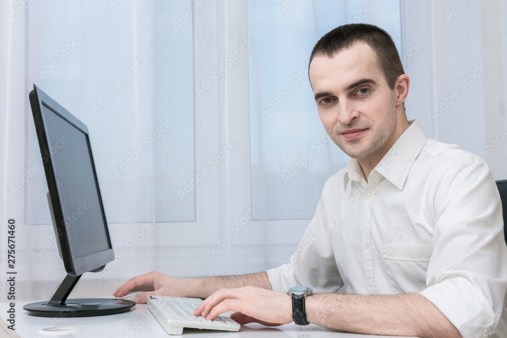 Clerk working in the office at the computer, looking at the camera