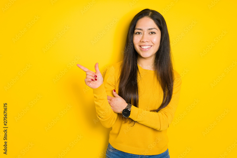 Beautiful brunette woman over yellow isolated background with a big smile on face, pointing with hand and finger to the side looking at the camera. Beautiful brunette woman over yellow isolated background with a big smile on face, pointing with hand and finger to the side looking at the camera.