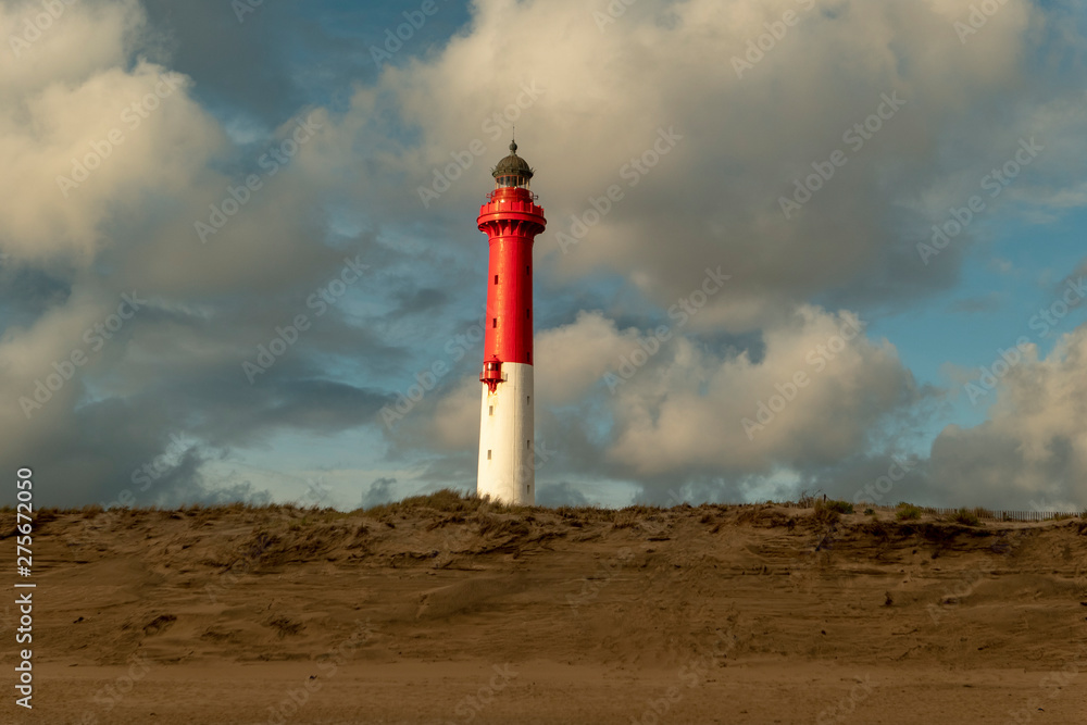 white red lighthouse with clouds at the sandy beach behind the dune