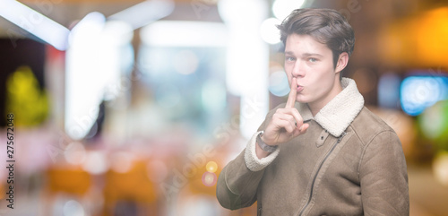 Young handsome man wearing winter coat over isolated background asking to be quiet with finger on lips. Silence and secret concept.