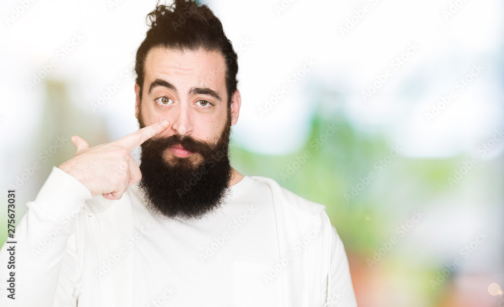 Young hipster man with long hair and beard wearing sporty sweatshirt Pointing with hand finger to face and nose, smiling cheerful Young hipster man with long hair and beard wearing sporty sweatshirt Pointing with hand finger to face and nose, smiling cheerful