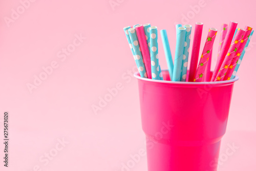 green and pink paper cocktail straws in plastic cup on a pink background. Concept: holiday, party, ecology, plastic
