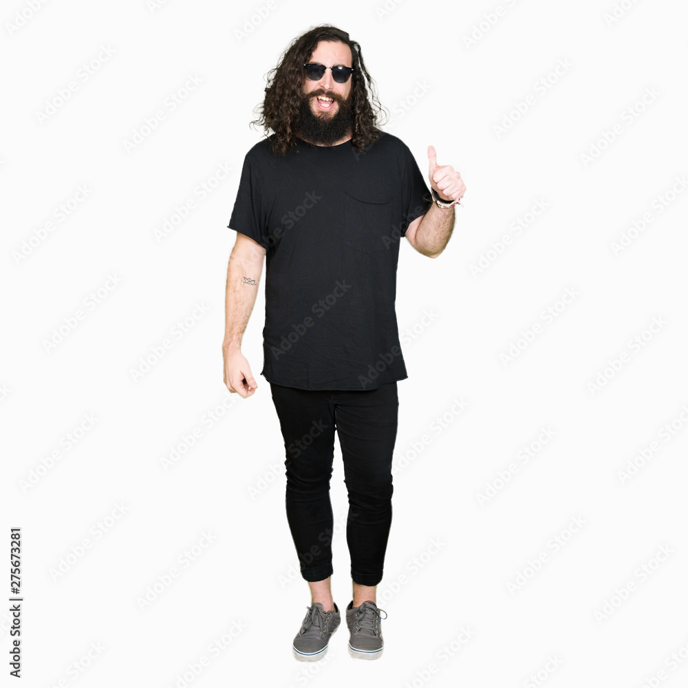 Young hipster man with long hair and beard wearing sunglasses doing happy thumbs up gesture with hand. Approving expression looking at the camera with showing success. Young hipster man with long hair and beard wearing sunglasses doing happy thumbs up gesture with hand. Approving expression looking at the camera with showing success.