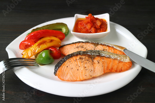 Healthy dish of grilled salmon steaks with colorful vegetables served on dark brown wooden table