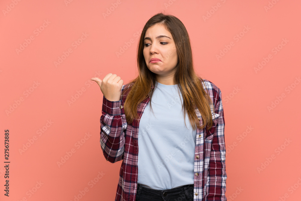 Young girl over pink wall unhappy and pointing to the side Young girl over pink wall unhappy and pointing to the side