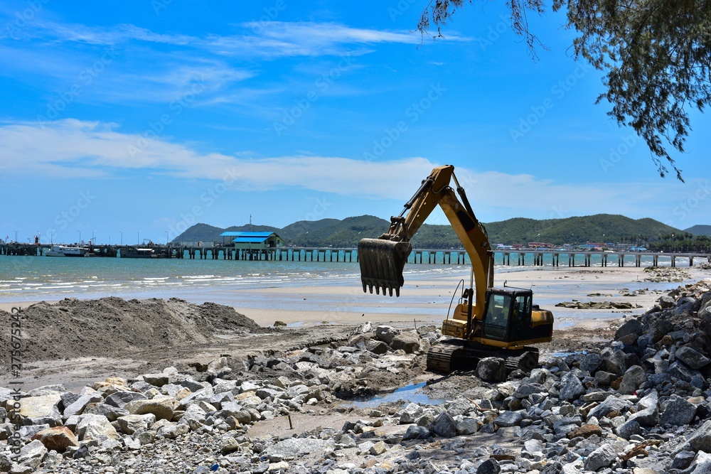 Fototapeta premium Crawler excavator are moving rocks to make breakwater on the beach. The beach , mountains and blue sky blackground