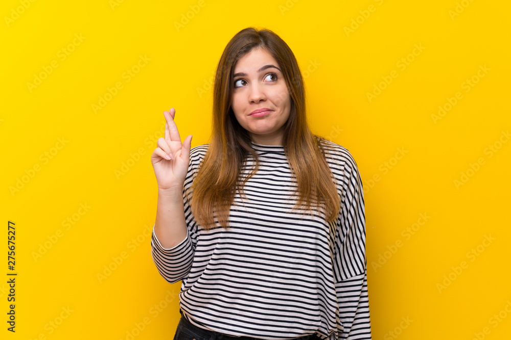 Young girl over yellow wall with fingers crossing and wishing the best Young girl over yellow wall with fingers crossing and wishing the best