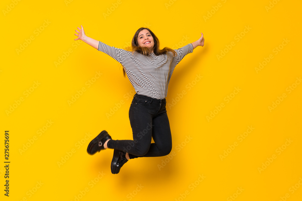 A full-length shot of a Young girl  jumping over isolated yellow background