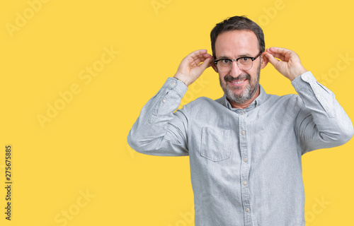 Handsome middle age elegant senior man wearing glasses over isolated background Smiling pulling ears with fingers, funny gesture. Audition problem