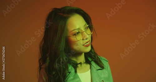 Close up of the attractve young Asian woman in glasses smiling and dreaming cheerfully on the red and orange neon background. photo