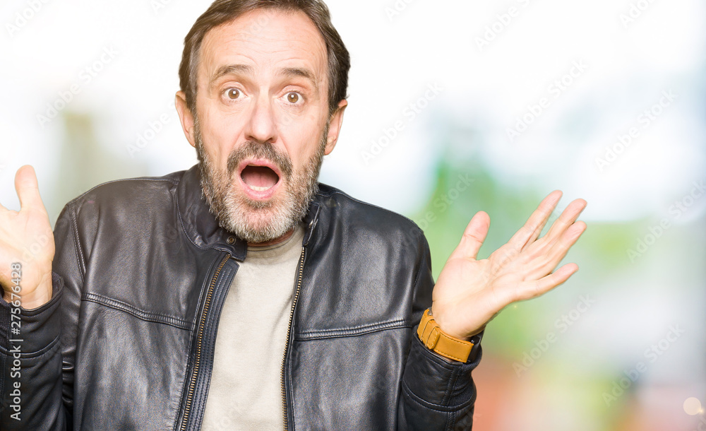 Middle age handsome man wearing black leather jacket clueless and confused expression with arms and hands raised. Doubt concept. Middle age handsome man wearing black leather jacket clueless and confused expression with arms and hands raised. Doubt concept.