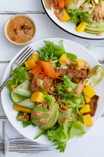 Healthy summer fresh salad with mango, avocado, lime and tofu with sweet peanut butter dressing on white wooden table