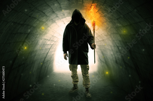 Ugly man with burning flambeau walking in a dark tunnel