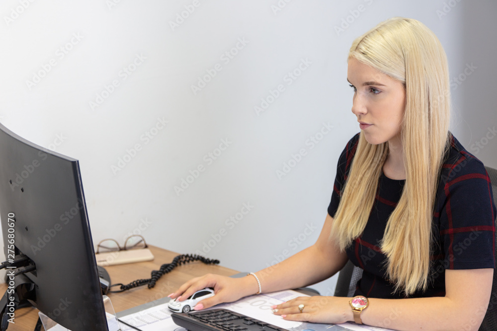 a young woman with long blond hair sits at a desk and enters data on a computer a young woman with long blond hair sits at a desk and enters data on a computer
