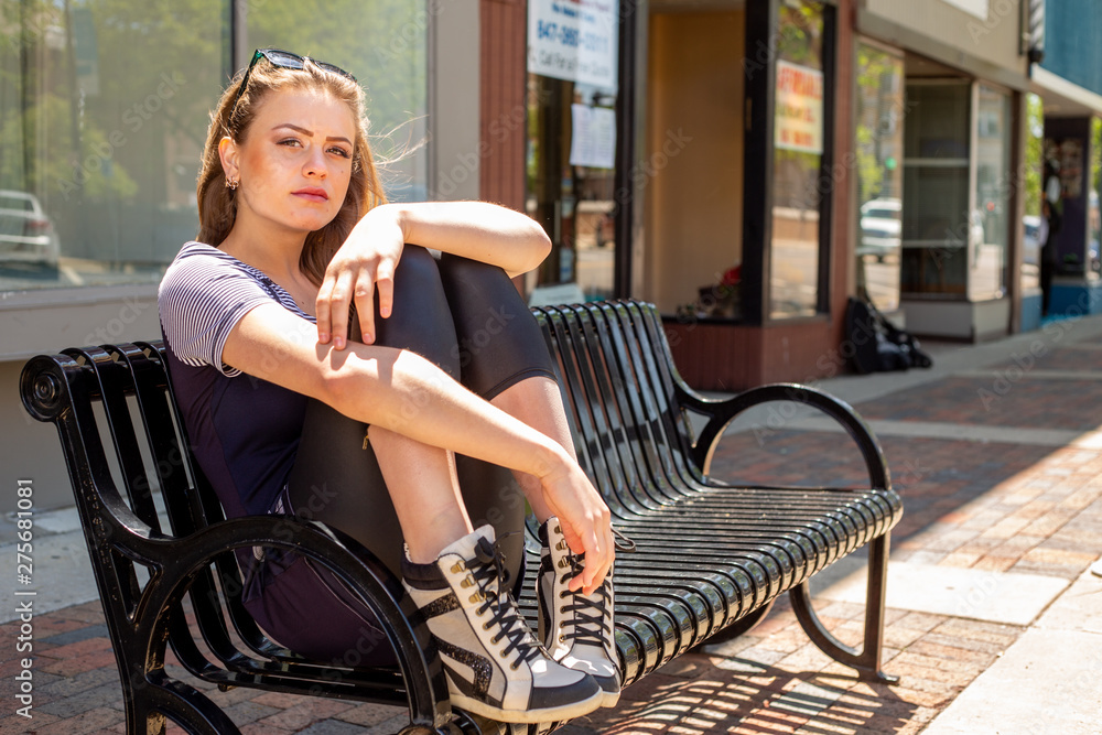 Young pretty white woman sitting on bench outside 