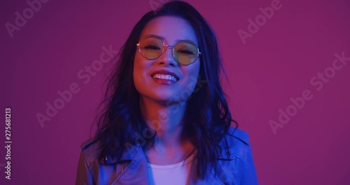 Wallpaper Mural Cute pretty young Asian stylish girl in sunglasses laughing cheerfully to the camera and fixing her hair witha hand on the pink neon background. Close up. Portrait. Torontodigital.ca