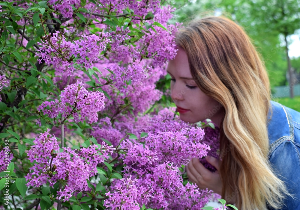Young blond woman by the blooming bush of purple lilac Young blond woman by the blooming bush of purple lilac