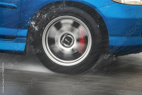 Detail of the rear wheel of a car driving in the rain on a wet road. Aquaplaning in road traffic. © milkovasa
