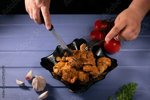 Baked chicken in a dark plate on a blue wooden background with dill, tomatoes, garlic, with a knife and fork in hand. photo