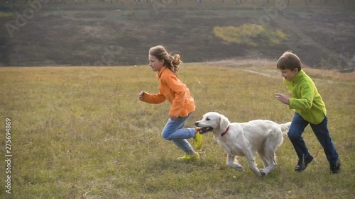 Two kids running with golden retriever at field