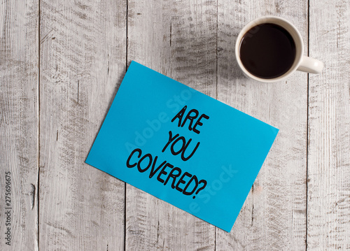 Text sign showing Are You Covered Question. Business photo showcasing asking showing if they had insurance in work or life Pastel Colour paper placed next to a cup of coffee above the wooden table