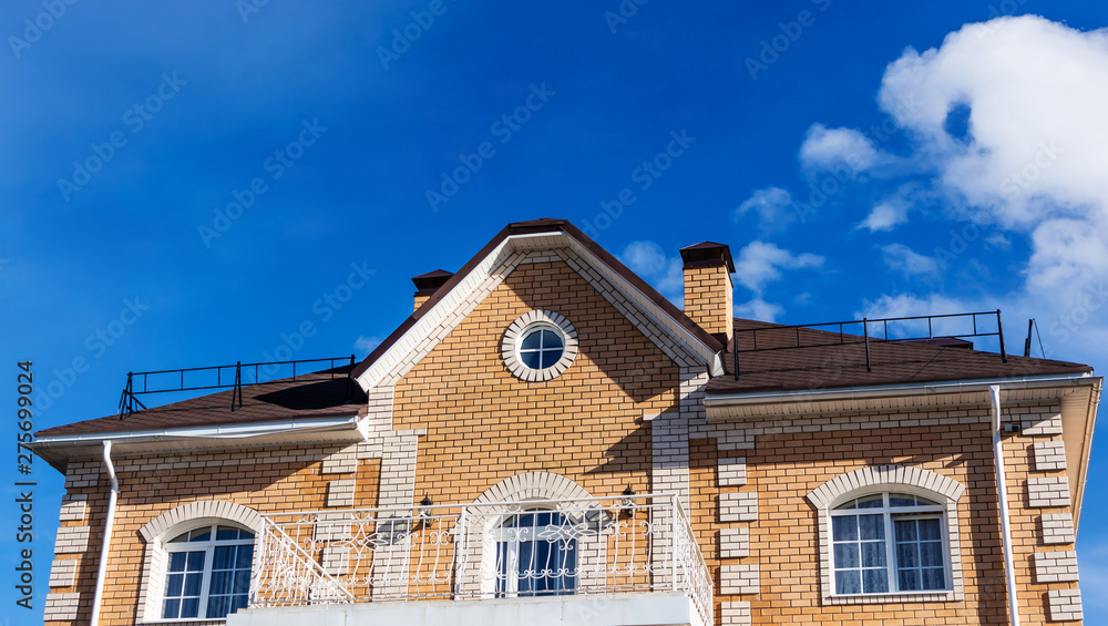 The roof windows and balcony of the house is pastel yellow and brown against a blue sky with light clouds. Bright sunny daylight. Place for text, minimalism. The concept of building houses, cottages. The roof windows and balcony of the house is pastel yellow and brown against a blue sky with light clouds. Bright sunny daylight. Place for text, minimalism. The concept of building houses, cottages.