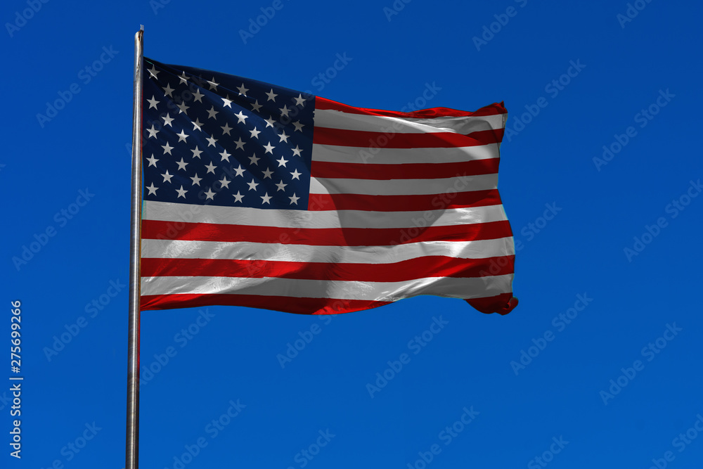 Flag of USA waving in the wind on flagpole against the sky with clouds on sunny day, banner, close-up