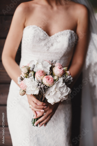The bride in an elegant wedding dress holds a beautiful bouquet of different flowers and green leaves. Wedding theme